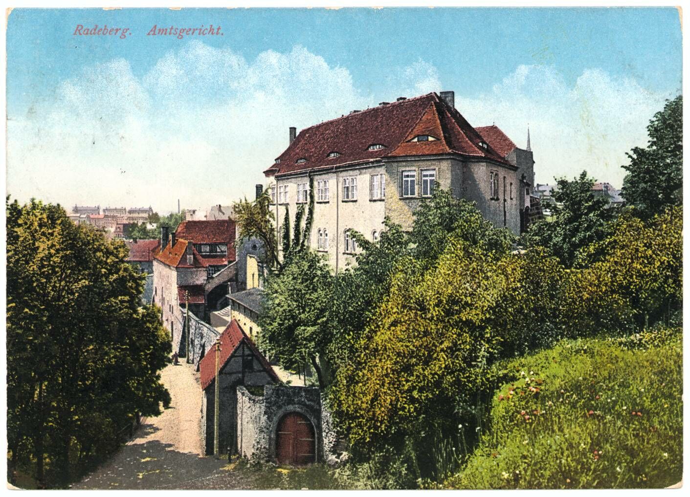 Foto in Vergrößerungsansicht öffnen: Blick auf den hinteren Schlosseingang, die Hauptburg, die Schlossmauer und den Weg, der an der Schlossmauer entlang führt. Es handelt sich um eine kolorierte Postkarte von 1915.