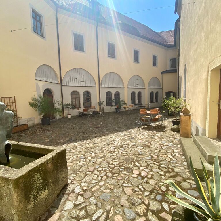 Blick in den Oberen Schlosshof im Sommer - von Mauern umschlossener gepflasterter Innenhof mit Brunnen, Palmen und Sitzgelegenheiten