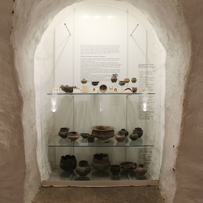 In einer hohen tiefen Wandnische befindet sich die Vitrine zum Thema Archäologie mit verschiedenen Fundstücken auf drei Ebenen..