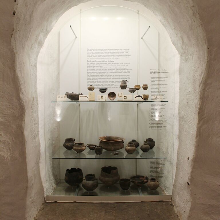 In einer hohen tiefen Wandnische befindet sich die Vitrine zum Thema Archäologie mit verschiedenen Fundstücken auf drei Ebenen..