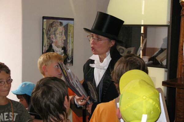 Der Dichter Langbein mit Zylinder und schwarzem Frack führt die Kinder durch das Schloss.