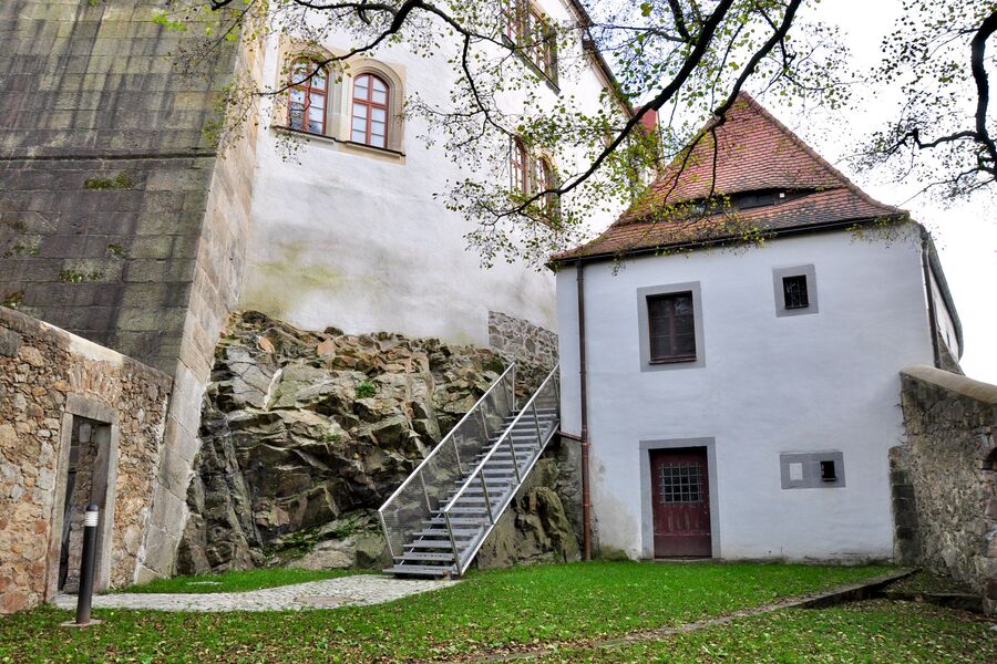 Farbiges Foto mit Blick auf eine Rasenfläche, das Gefängnisgebäude und eine neue Stahltreppe, die zur Hauptburg führt