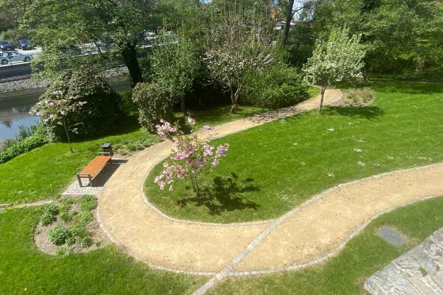 Blick auf den Rundweg im Schlossgarten mit blühenden Bäumen und einer Bank unterhalb des Schlossteiches