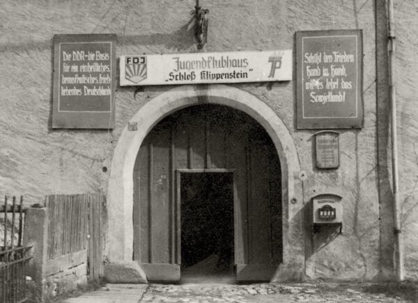 vorderer Eingang zum Schloss Klippenstein mit Schild 'Jugendclubhaus Schloss Klippenstein' und politischen Parolen der DDR an der Wand