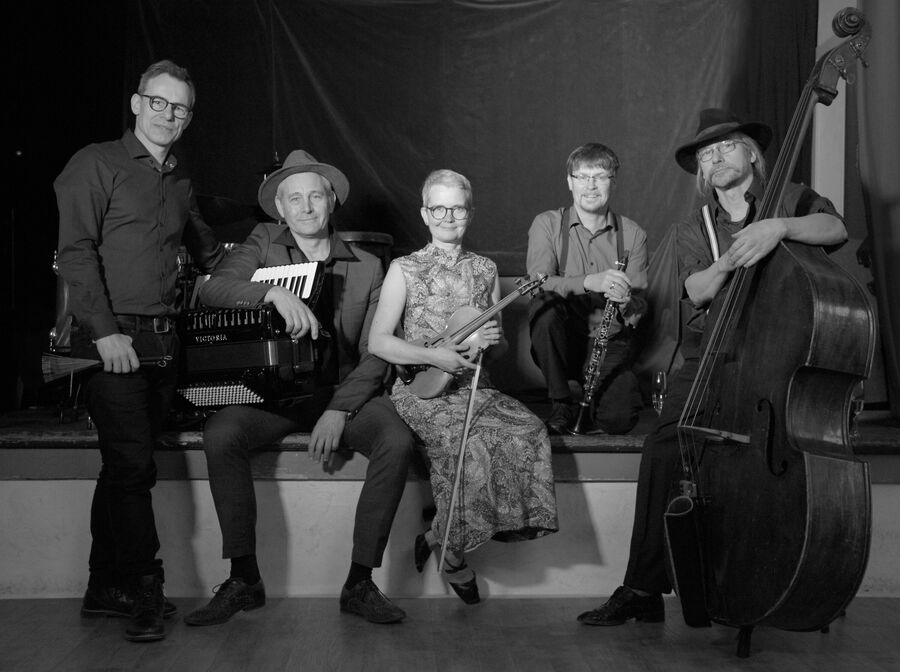 Fünf Musiker der Gruppe Klezmart sitzen und stehen vor schwarzem Hintergrund mit Akkordeon, Geige, Klarinette und Kontrabass