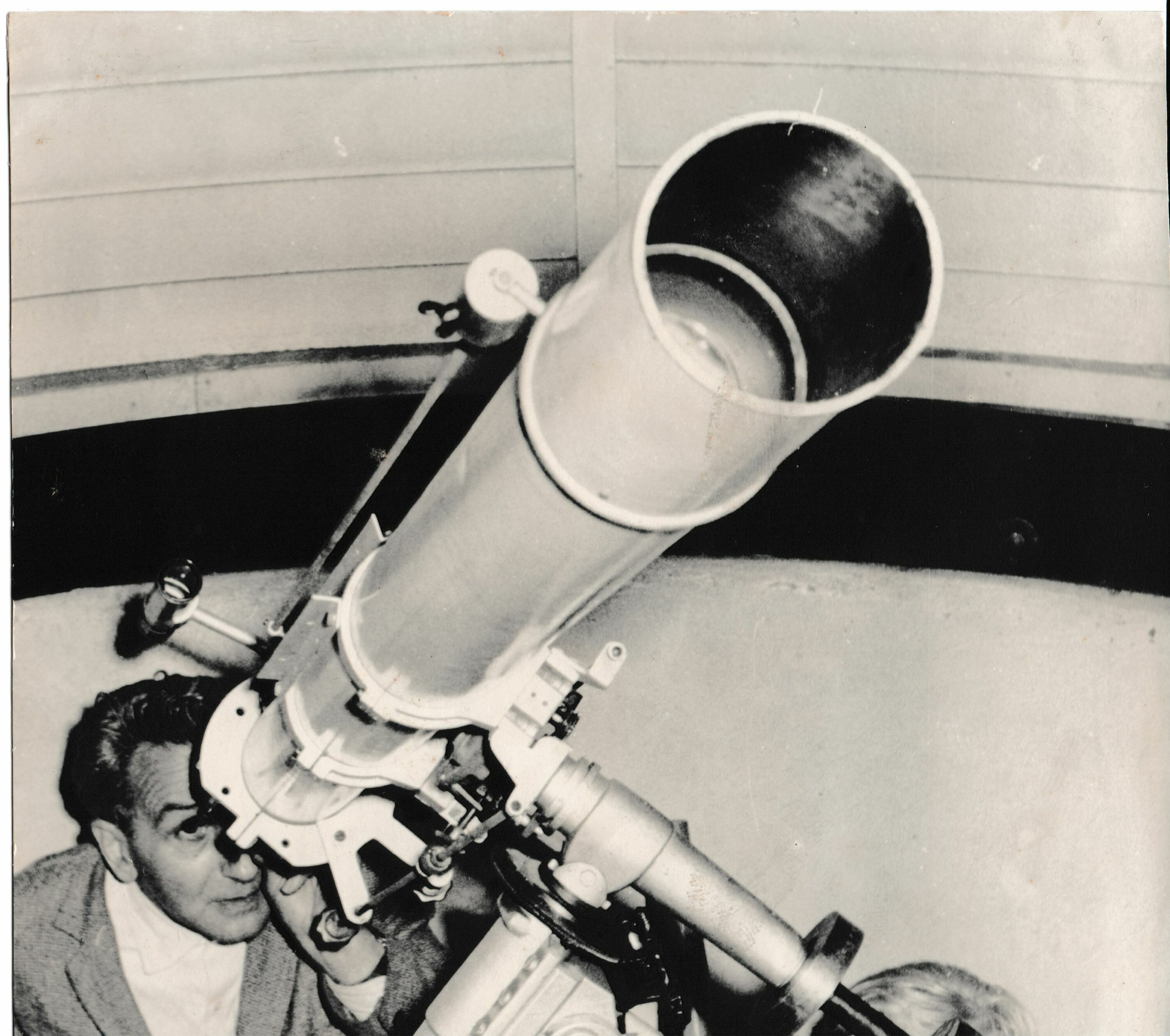 Foto in Vergrößerungsansicht öffnen: Schrzweiß-Foto von 1965. Erich Bär, Leiter der Volkssternwarte, schaut in der linken unteren Bildecke in ein durch die Aufnahmeperspektive riesig erscheinendes Fernrohr, welches diagonal nach rechts oben das gesamte Bild einnimmt.
