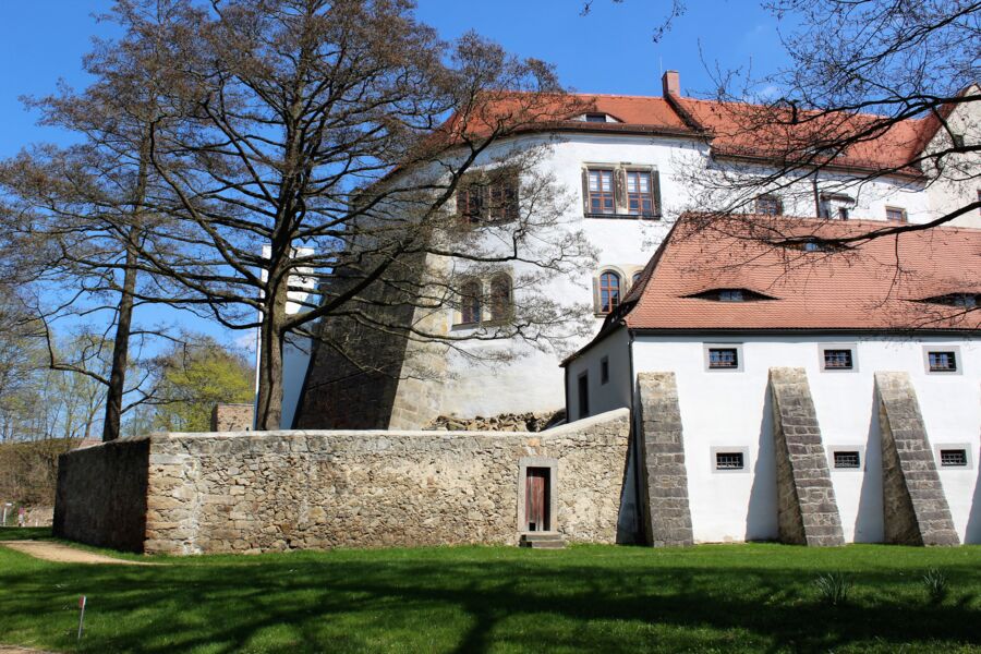 Blick vom Schlossgarten auf die weißen Fassaden und roten Ziegeldächer der Vorburg und der Nordseite der Hauptburg sowie auf die Bruchstein-Umfassungsmauern des Gefängnishofes.