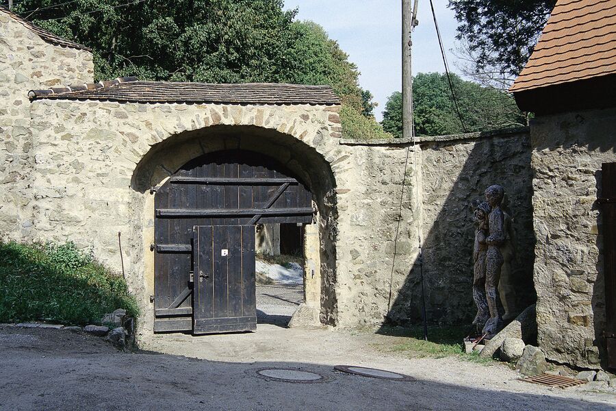 Farbfoto mit Blick vom unteren Schlosshof auf das offene Tor am Eulenturm, rechts vom Tor stehen zwei Skulpturen
