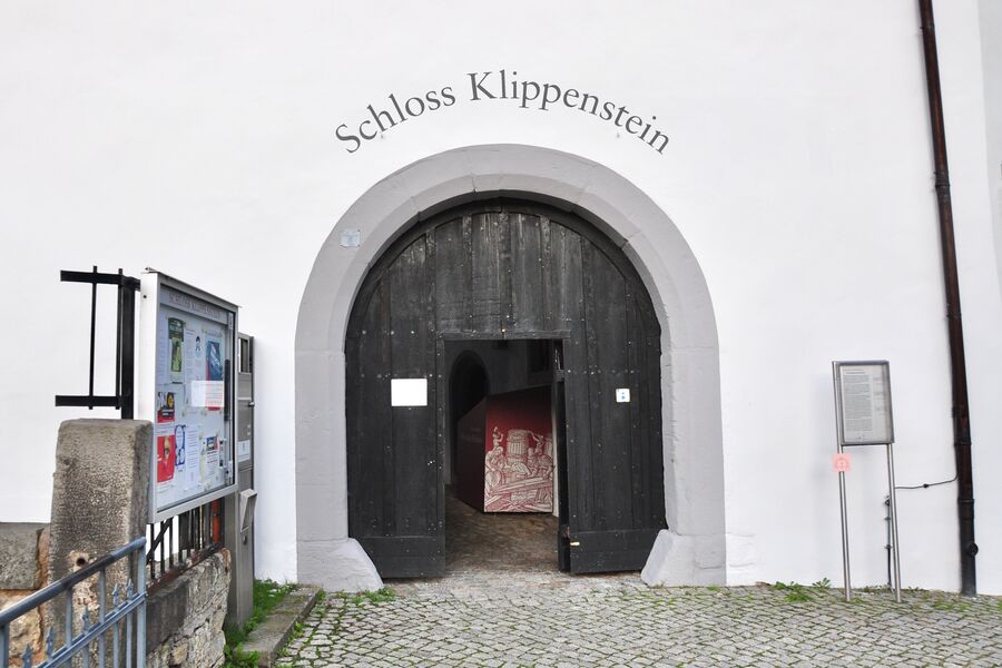 Farbfoto mit dem stadtseitigen Tor aus Holz mit Rundbogen und offener Tür und dem Schriftzug "Schloss Klippenstein"