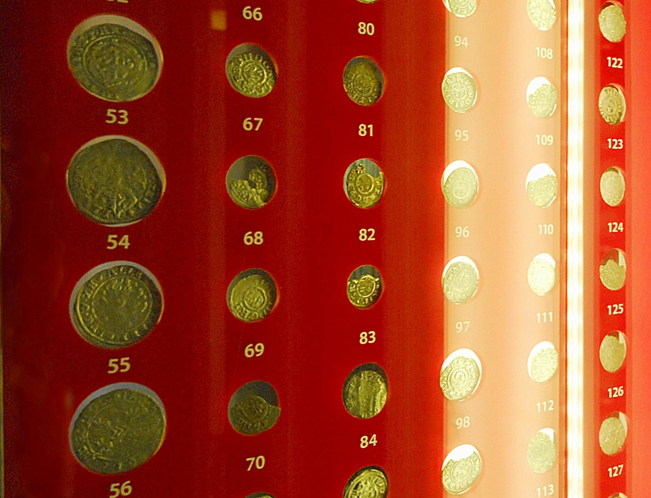 Detailansicht einer Ausstellungsvitrine mit Münzen vor rotem Hintergrund in der Schatzkammer des Museums.