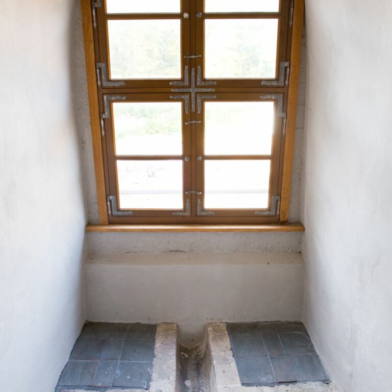 Vor einem Fenster sieht man eine kurze Abflussrinne mit einem sich anschließenden flachen Becken aus Stein.