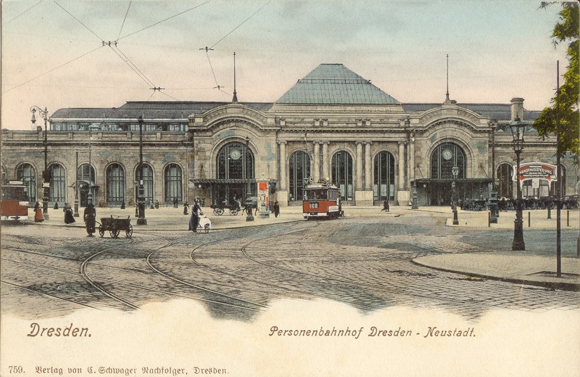 Foto in Vergrößerungsansicht öffnen: die kolorierte querformatige Ansichtskarte zeigt über die ganze Breite das Empfangsgebäude des Bahnhofes Dresden-Neustadt. Davor sind eine rote Straßenbahn und Passanten zu sehen.