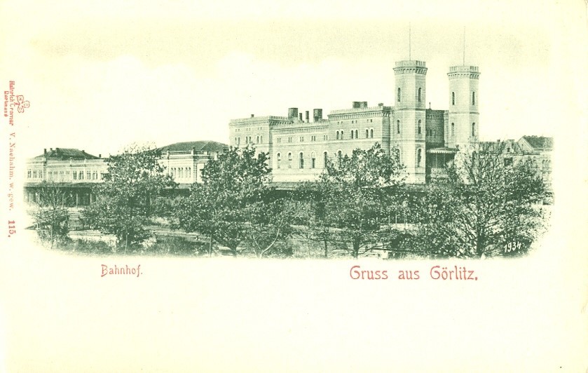 Foto in Vergrößerungsansicht öffnen: Eine grünstichige Schwarzweiß-Aufnahme auf einer Ansichtskarte, die durch eine Parkanalege den Blick auf den herrschaftlichen Bahnhof Görlitz mit seinen zwei Türmen zeigt.