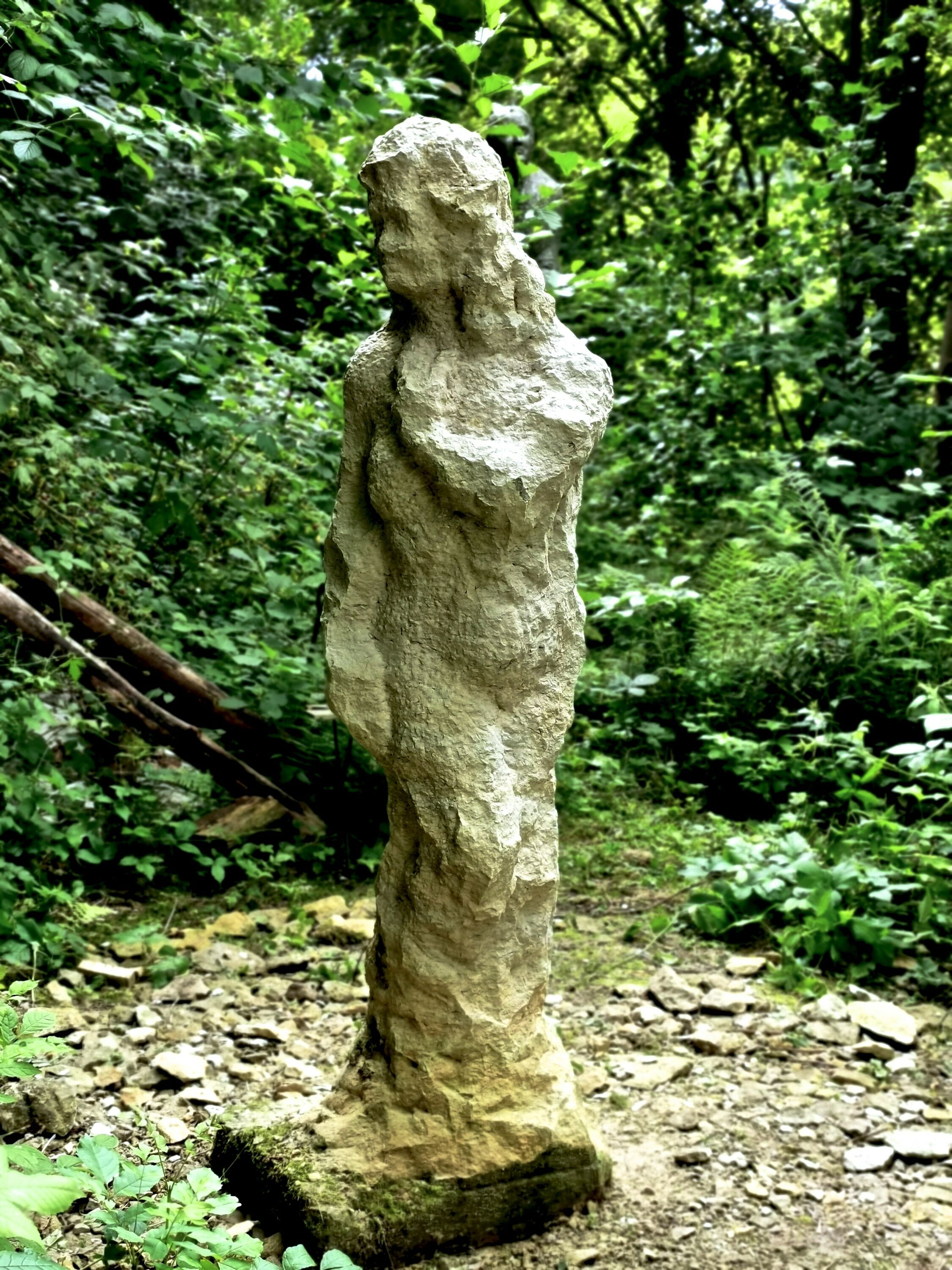 Sandsteinfigur einer schlanken Frau steht in einem Park. Die Skulptur heißt Moira und wurde 2022 hergestellt.